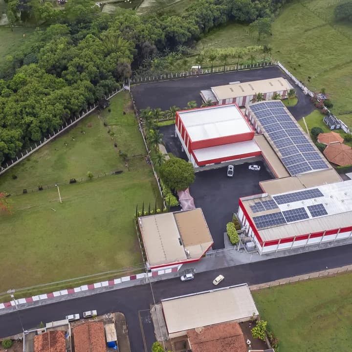 A fábrica vista de longe, cercada de mata e pasto, com a estrada de acesso