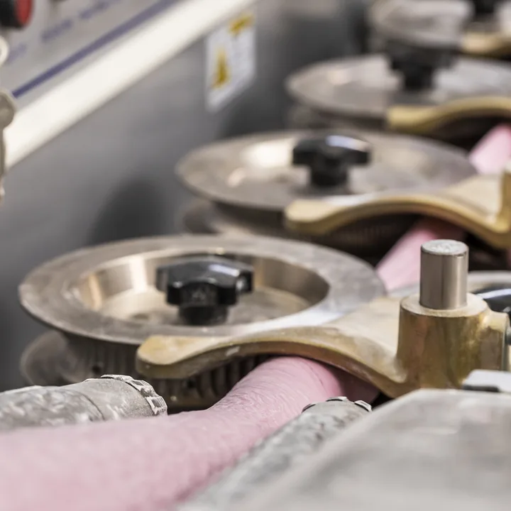 Close dos moldes de bronze que dão forma à bala, com a massa rosa passando entre eles