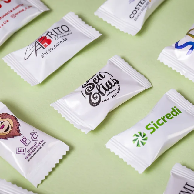 Balas em embalagem branco pérola com marcas de clientes impressas, sobre fundo verde claro