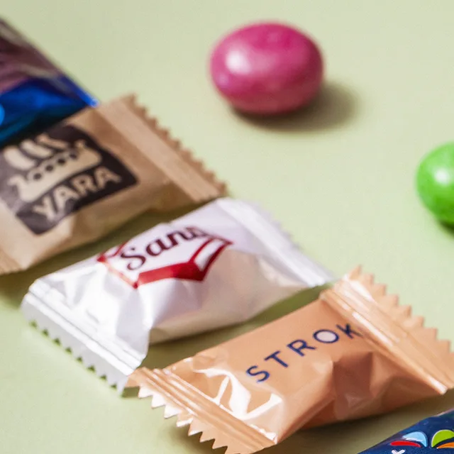 Sachês de papel kraft com marca impressa, ao lado de drops coloridos