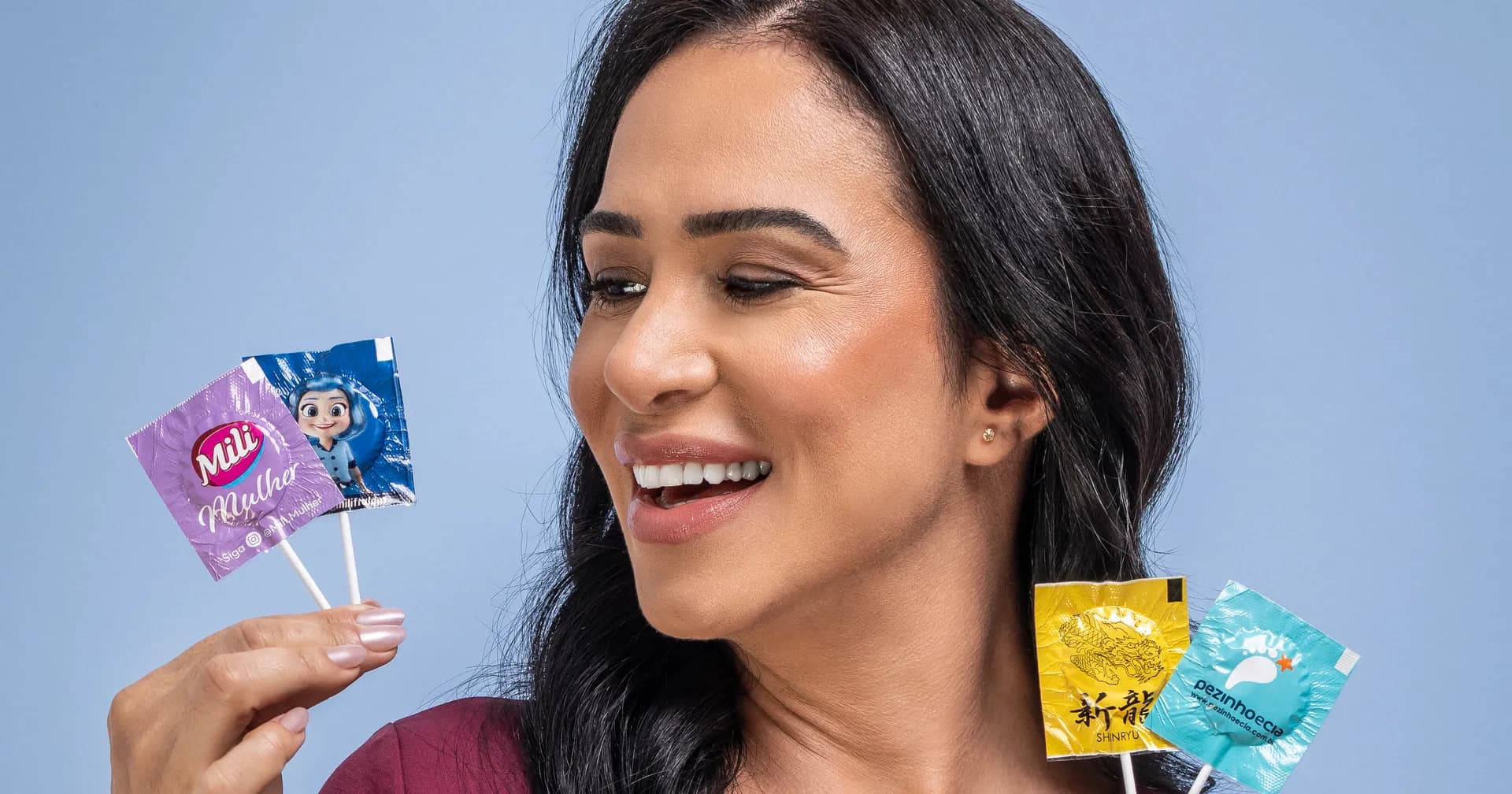 Mulher sorrindo segura quatro pirulitos FrutPop com embalagens personalizadas de marcas diferentes