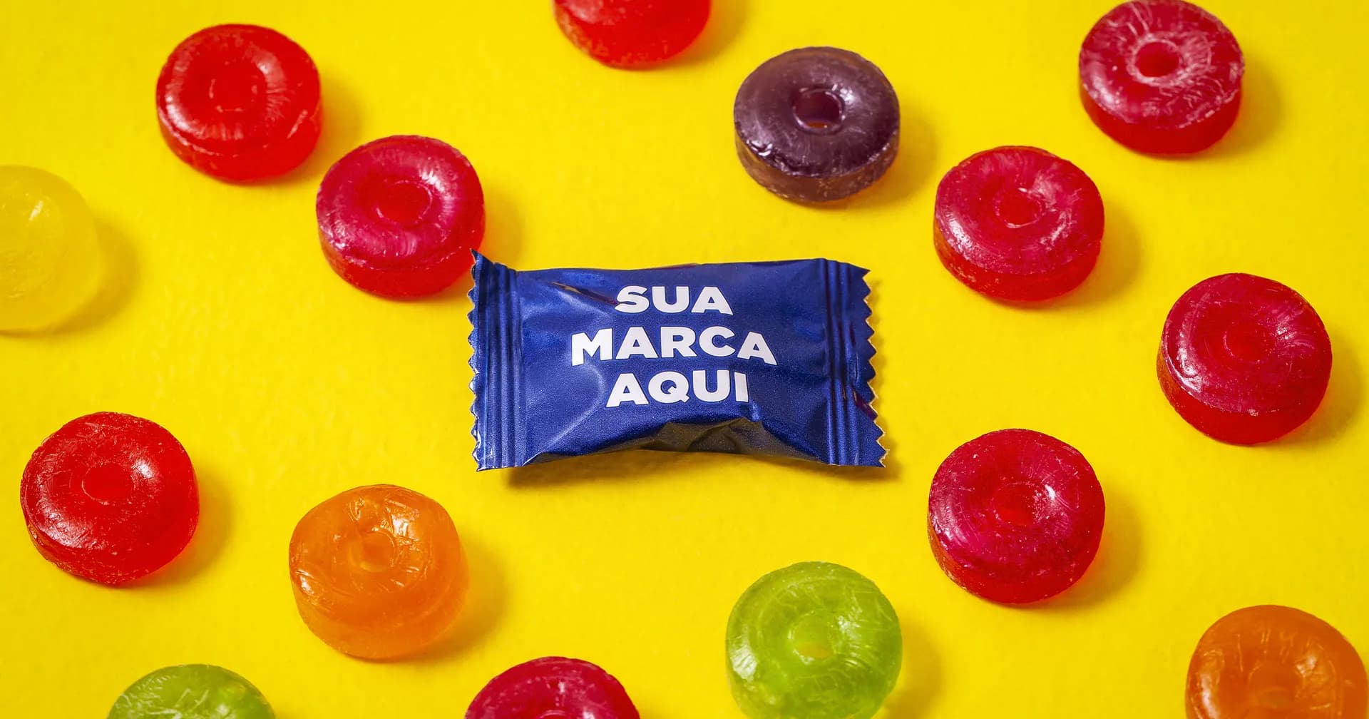 Bala azul personalizada com a frase Sua Marca Aqui na embalagem, cercada de balas coloridas sobre fundo amarelo