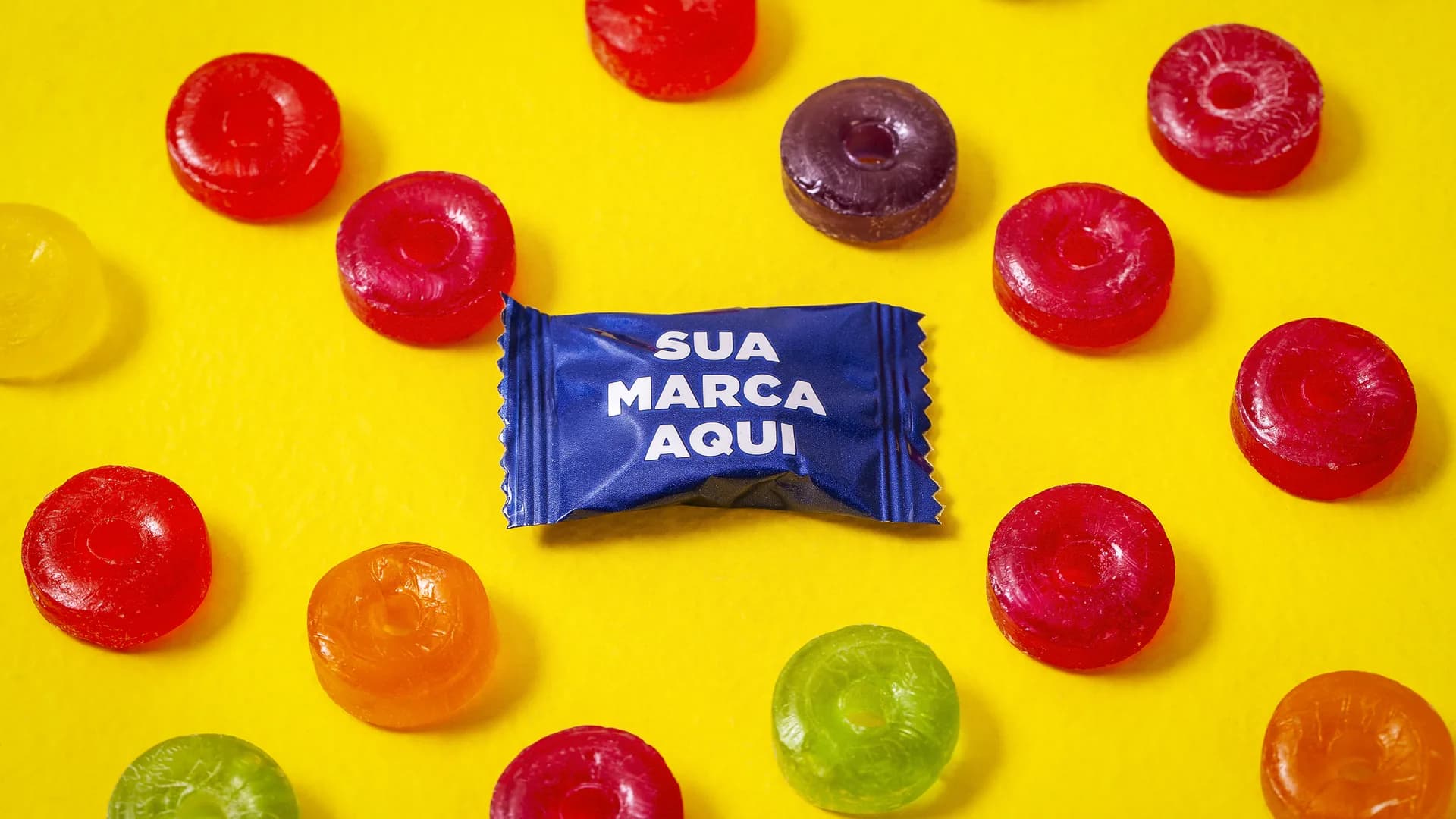 Bala com embalagem azul escrita Sua Marca Aqui, cercada de balas coloridas sobre fundo amarelo