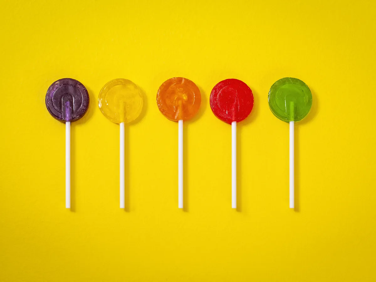 Cinco pirulitos FrutPop coloridos sobre fundo amarelo